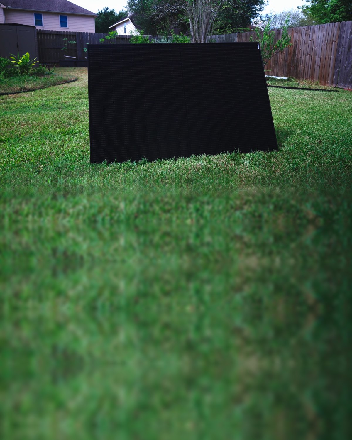 A single solar panel in a fenced backyard
